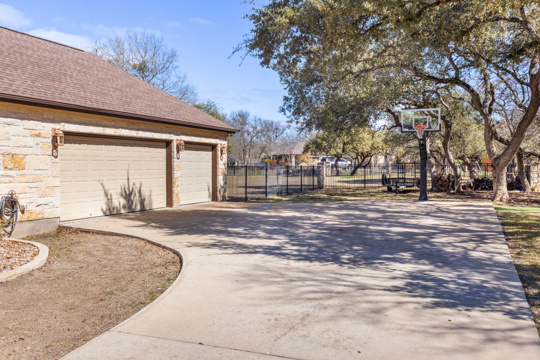 Two-car garage with extended driveway and basketball court under oak trees