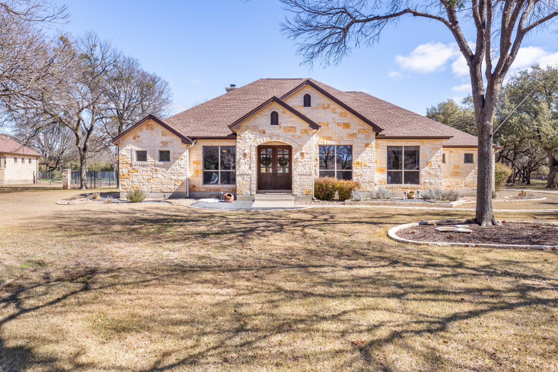 Custom Hill Country estate at 104 Roble Roja Dr Georgetown TX - stone and stucco exterior with mature oak trees at golden hour