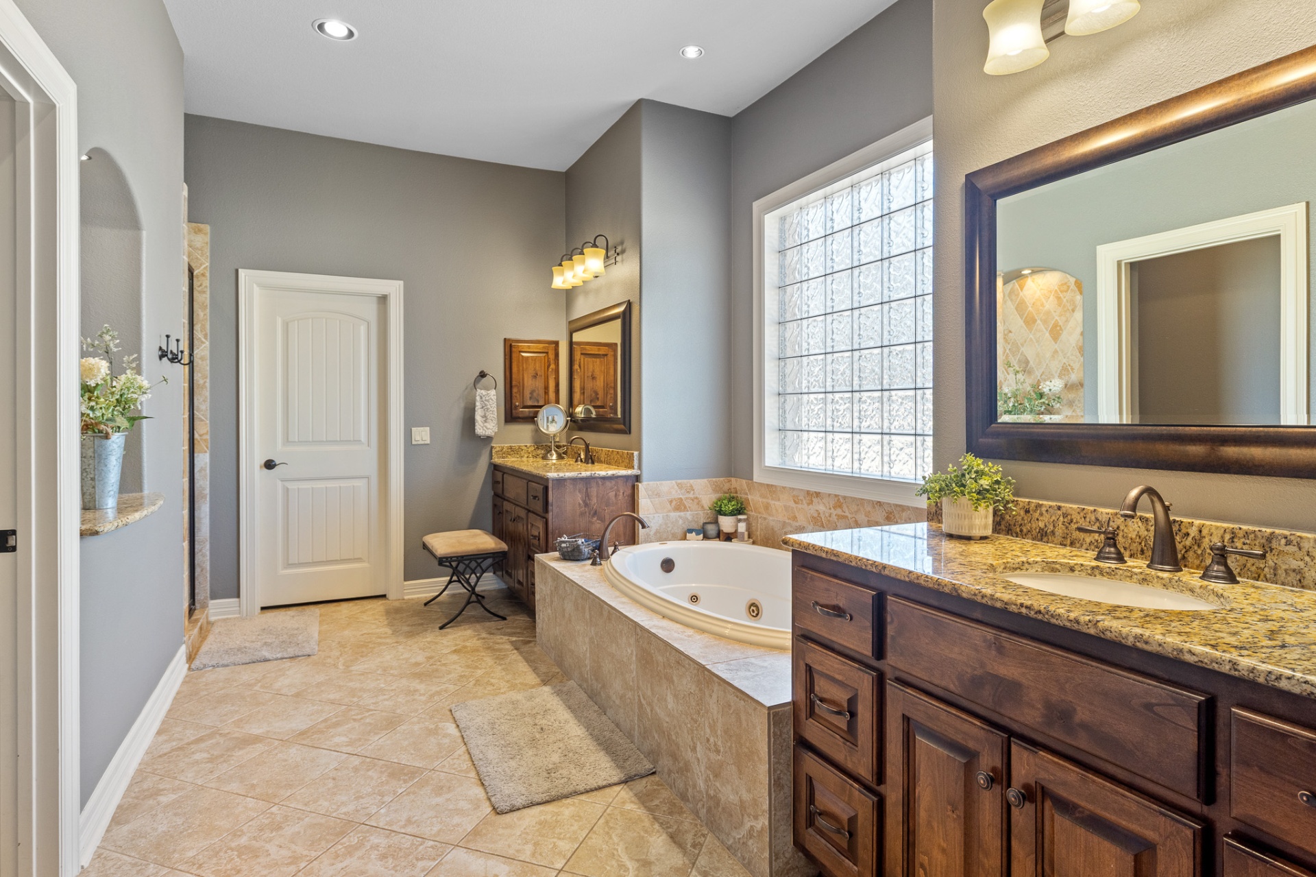 Primary bathroom with dual vanities, soaking tub, and glass block window