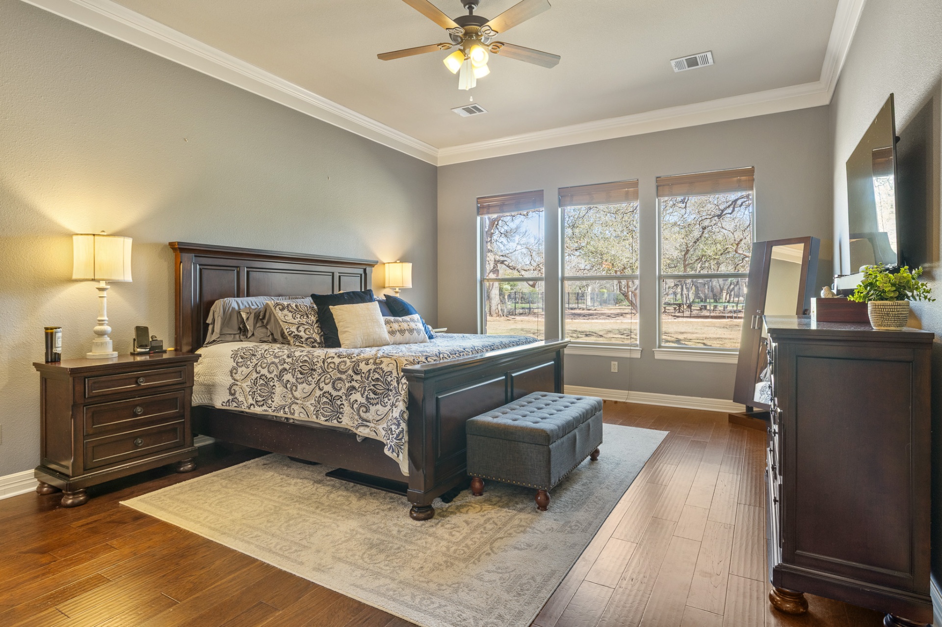 Primary bedroom with hardwood floors and triple windows overlooking oak trees