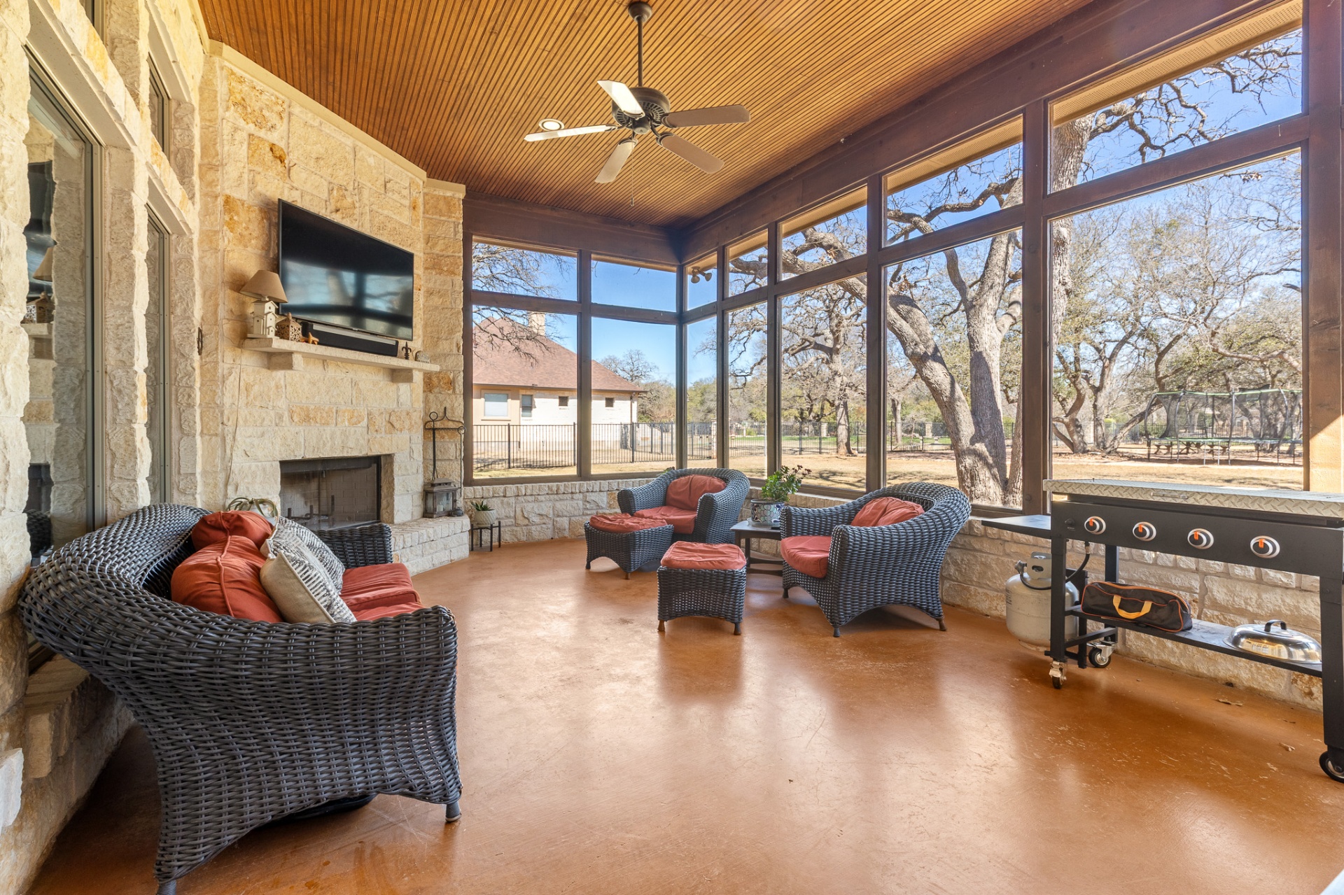 Screened patio with stone fireplace, TV, wicker seating and outdoor grill
